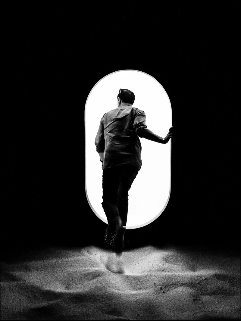 Photographie noir et blanc d'un homme qui rentre par une porte blanche aux bords arrondis
